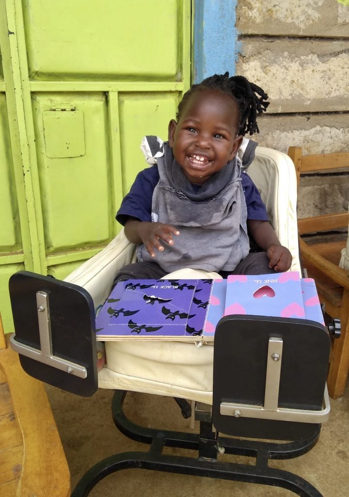 little girl in her sitting aid, laughing and reading a book